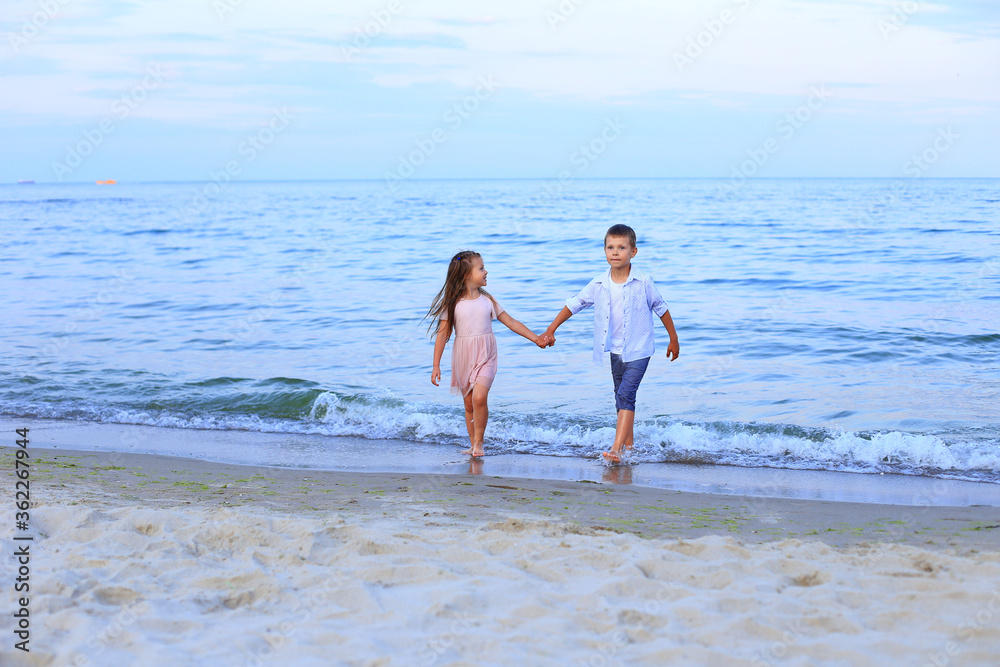 Two children run along the sea near the shore