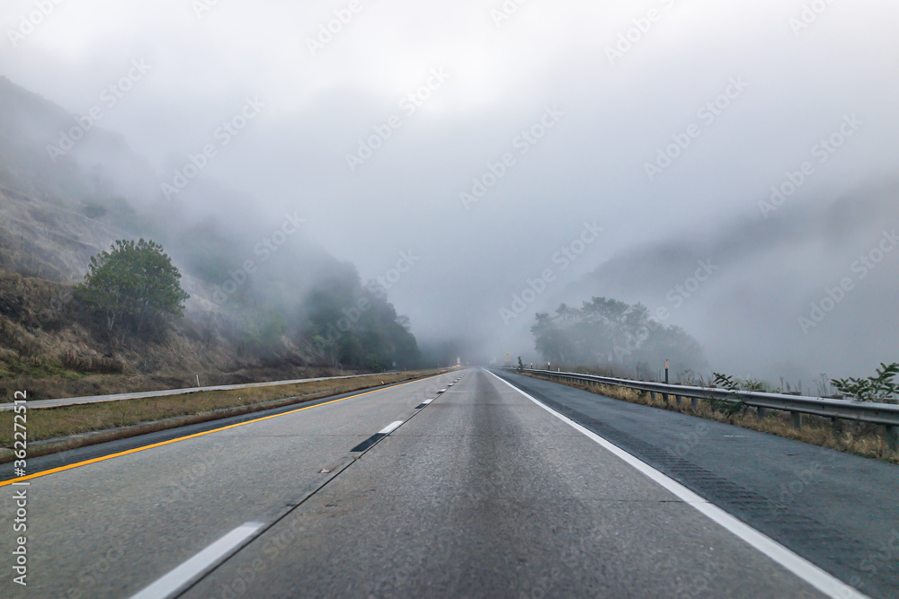 Fog mist road highway driving pov point of view in rural countryside in West Virginia through grey clouds on steep paved way Fog mist road highway driving pov point of view in rural countryside in West Virginia through grey clouds on steep paved way