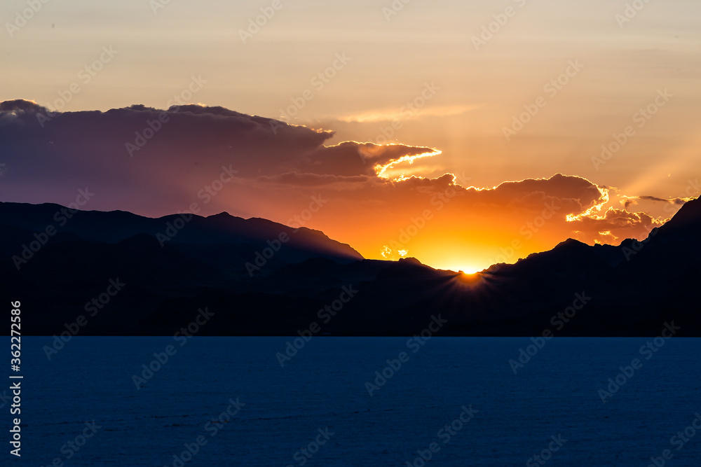 Bonneville Salt Flats dark blue landscape near Salt Lake City, Utah and silhouette mountain view and sunset sun rays glowing behind clouds