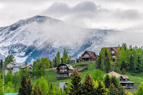 Crested Butte, USA Colorado town village in summer with clouds and foggy mist morning and houses on hillside with green trees