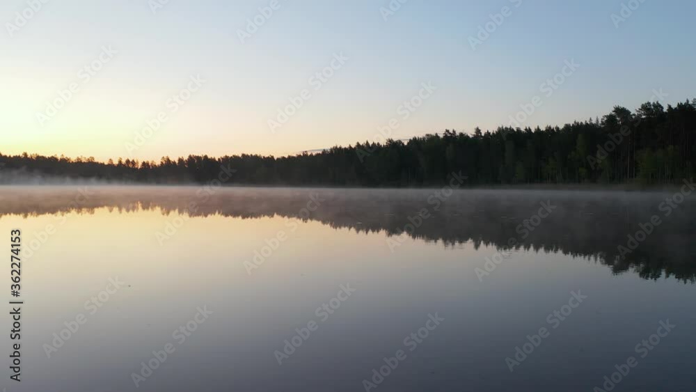 Flying over lake at dawn. Early morning mist above water. Beautiful sunrise, clear sky, calm water and forest. Sunlight and forest reflected in the water. Camera forward movement. 4k footage. Flying over lake at dawn. Early morning mist above water. Beautiful sunrise, clear sky, calm water and forest. Sunlight and forest reflected in the water. Camera forward movement. 4k footage.