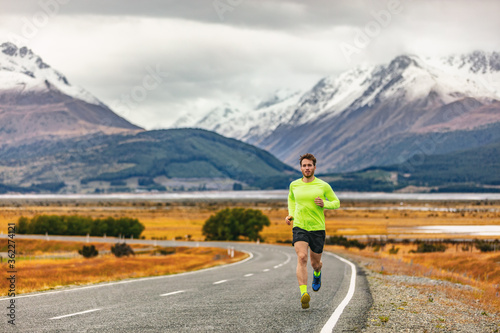 Athlete runner running road race in amazing mountain range landscape in New Zealand. Man run exercise long distance cardio training outdoors in cold fall weather.