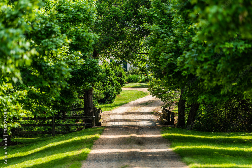 Gated open entrance with bridge over river with road driveway in rural countryside in Virginia estate gravel dirt path street with green lush trees in summer