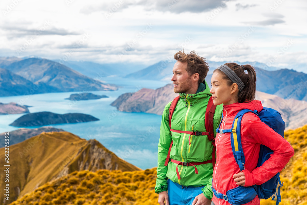 Hiking couple wanderlust adventure and travel concept with hikers relaxing looking at view. Hiking couple tramping up famous hike to Roys Peak on South Island, New Zealand.