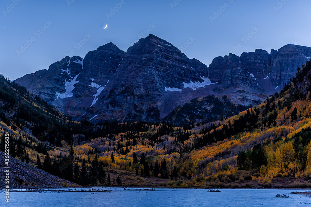 Maroon Bells in October 2019 lake peak view blue hour in Aspen, Colorado at dark night with rocky mountains and fall autumn foliage with moon in sky