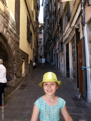A cheerful girl in a yellow hat in the narrow street of Genoa Italy