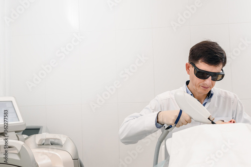 Male cosmetologist doing laser epilation treatment in spa salon