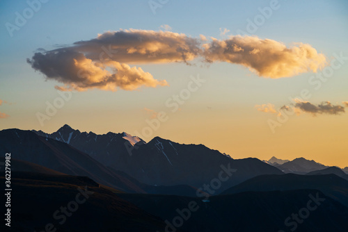Colorful dawn landscape with beautiful mountains silhouettes and golden blue gradient sky with clouds. Vivid mountain scenery with picturesque multicolor sunset. Scenic sunrise view to mountain range.