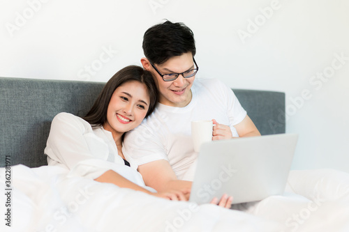 Young asian couple love man and woman watching movie in laptop on the bed in the morning. Happy moment concept.