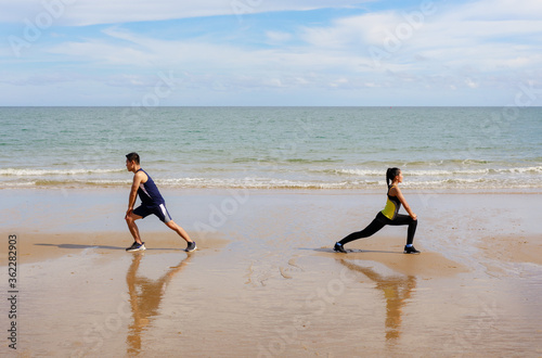 A Asian couple training on beach stretching before work out. Young man and woman during summer workout.