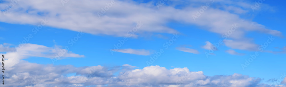 Bright blue sky with white clouds, illuminated by the sun. Beautiful summer landscape.Wide format, panorama