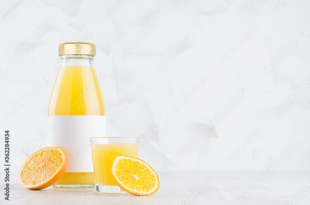 Fresh juicy orange juice in glass bottle with blank label mock up with wine glass decorated fruit slices in soft light white interior on wood table with copy space. Fresh juicy orange juice in glass bottle with blank label mock up with wine glass decorated fruit slices in soft light white interior on wood table with copy space.