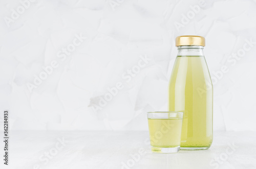 Fresh vegetable fruit green juice in glass bottle mock up with glass on wood table in white interior, template for packaging, advertising, design product, branding identity.