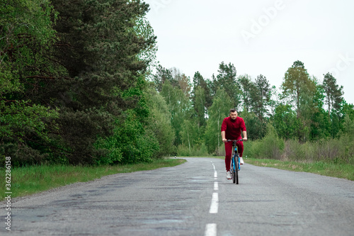 A man in a tracksuit on a bicycle rides on a road in the forest. The concept of a healthy lifestyle, cardio training. Copyspace.