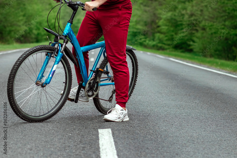 A man in a tracksuit stands next to a bicycle on a road in the forest. The concept of a healthy lifestyle, cardio training. Copyspace. A man in a tracksuit stands next to a bicycle on a road in the forest. The concept of a healthy lifestyle, cardio training. Copyspace.