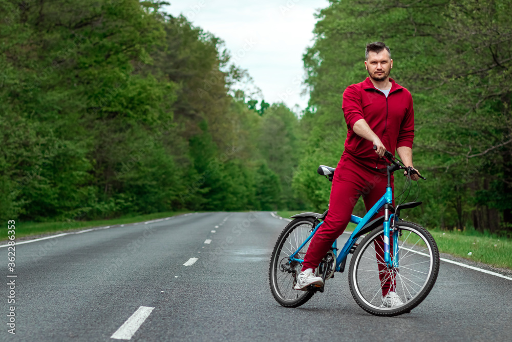 A man in a tracksuit stands next to a bicycle on a road in the forest. The concept of a healthy lifestyle, cardio training. Copyspace. A man in a tracksuit stands next to a bicycle on a road in the forest. The concept of a healthy lifestyle, cardio training. Copyspace.