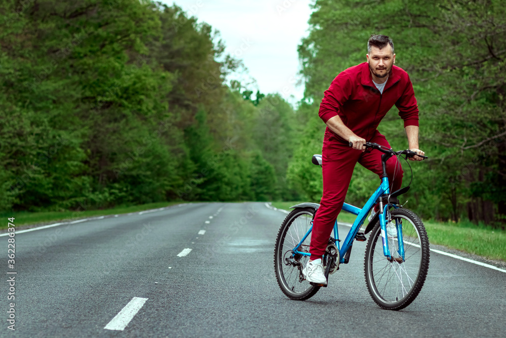 A man in a tracksuit on a bicycle rides on a road in the forest. The concept of a healthy lifestyle, cardio training. Copyspace. A man in a tracksuit on a bicycle rides on a road in the forest. The concept of a healthy lifestyle, cardio training. Copyspace.