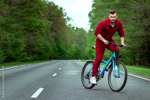 A man in a tracksuit on a bicycle rides on a road in the forest. The concept of a healthy lifestyle, cardio training. Copyspace.