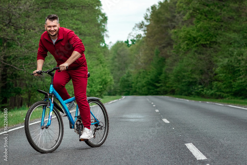 A man in a tracksuit on a bicycle rides on a road in the forest. The concept of a healthy lifestyle, cardio training. Copyspace.