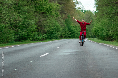 A man in a tracksuit rides a bicycle without hands on the road in the forest. The concept of a healthy lifestyle, cardio training. Copyspace.