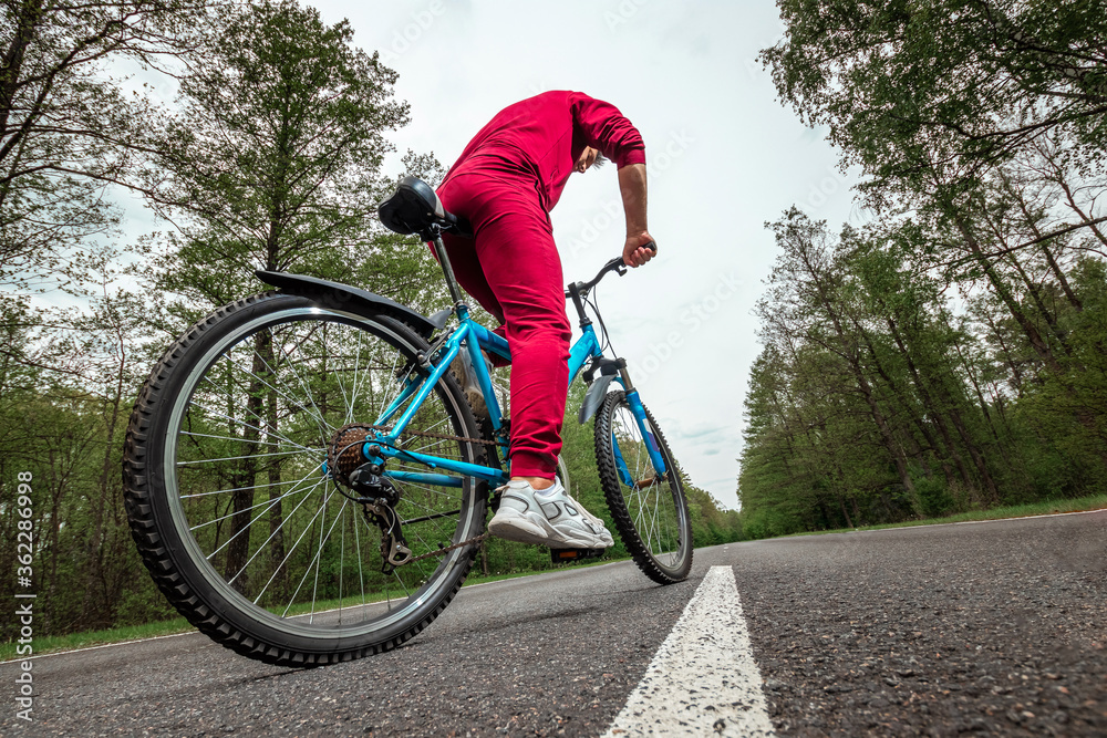 A man in a tracksuit on a bicycle rides on a road in the forest. The concept of a healthy lifestyle, cardio training. Copyspace.