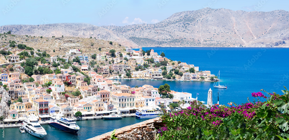 Panoramic view on tiny colorful houses on rocks and big boats on harbor near the Mediterranian sea on Greek island in sunny summer day, vacation on exotic islands