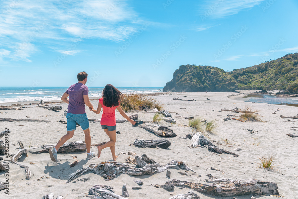Couple walking on beach in New Zealand running having fun holding hands - young romantic couple in Ship Creek on West Coast of New Zealand. Tourist couple sightseeing South Island of New Zealand.
