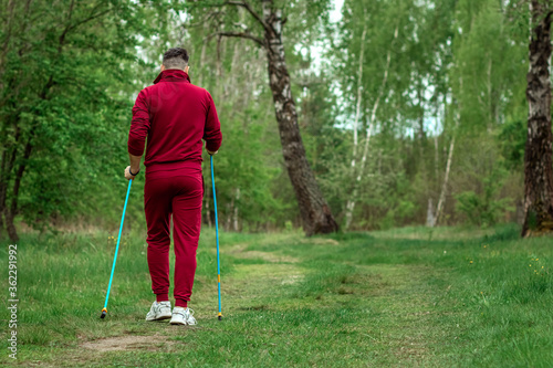 A man in a tracksuit is engaged in Nordic walking. The concept of a healthy lifestyle, cardio training. Copyspace.