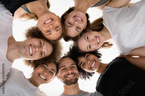 Close up head shot smiling beautiful mixed race people touching heads in circle, looking down at camera, healthy multiracial young teammates in sportwear feeling excited, waiting for training workout.