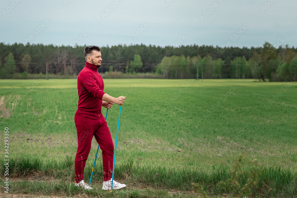 Fototapeta premium A man in a tracksuit is engaged in Nordic walking. The concept of a healthy lifestyle, cardio training. Copyspace.