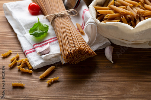 Whole grain uncooked pasta spaghetti and penne in cotton bag on wooden table