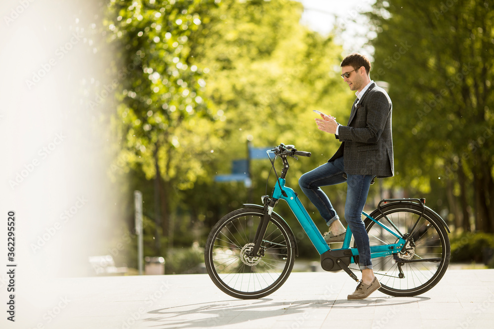 Obraz premium Young businessman on the ebike using mobile phone