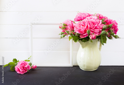 Photo frame and pink roses bouquet in vase. Empty  blank mock up, white board on background, poster product design