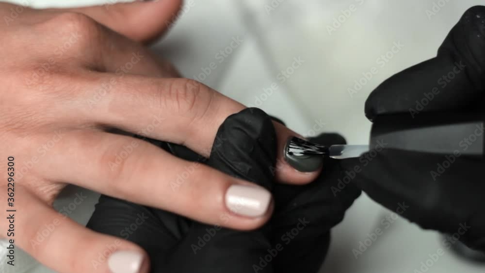 Close up of a beautician painting the middle finger with dark green nail polish
