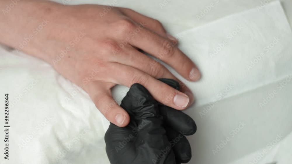 Looking down as a beautician paints a base coat onto a clients nails for a manicure Looking down as a beautician paints a base coat onto a clients nails for a manicure