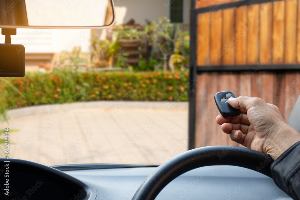 man inside red car, hand pressing remote control to open or close the electric sliding auto door.Home remote control, auto garage, security system in concept. man inside red car, hand pressing remote control to open or close the electric sliding auto door.Home remote control, auto garage, security system in concept.