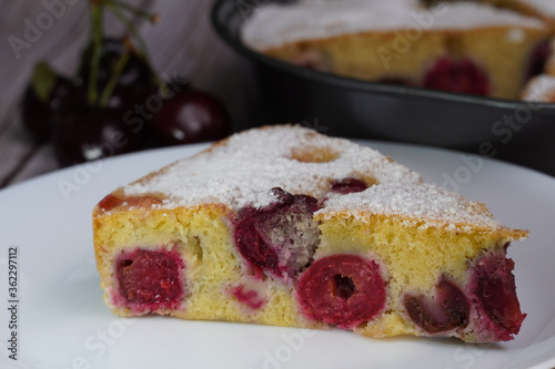 Piece of cherry pie with cherries in the left background