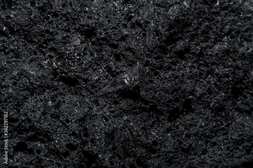 Blurred in soft focus at high magnification. Dark background with the texture of a piece of coal. The surface of fossil fuels with small decks and microcracks