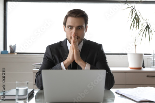 Stunned Caucasian male employee look at laptop screen shocked by unbelievable financial news on internet, amazed young businessman shocked by unexpected email or business message on computer