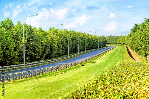 empty road landscape in city outskirts with pedestrian pathway against green forest background. Ground wide view of modern highway down to countryside. Street in town. Freeway in rural landscape