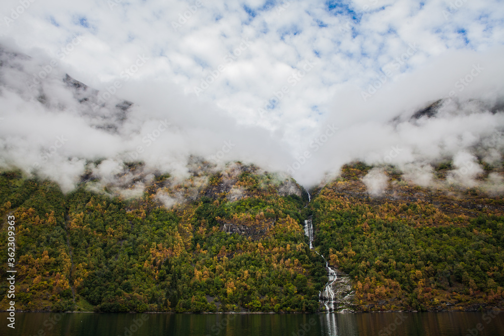 Low clouds over a waterfall in Geiranger fjord  in Norway