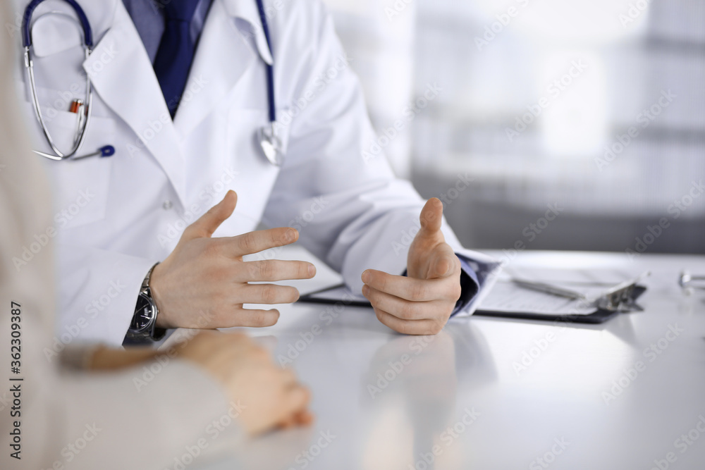 Unknown male doctor and patient woman discussing something while sitting in clinic and using clipboard. Best medical service in hospital, medicine, pandemic stop Unknown male doctor and patient woman discussing something while sitting in clinic and using clipboard. Best medical service in hospital, medicine, pandemic stop
