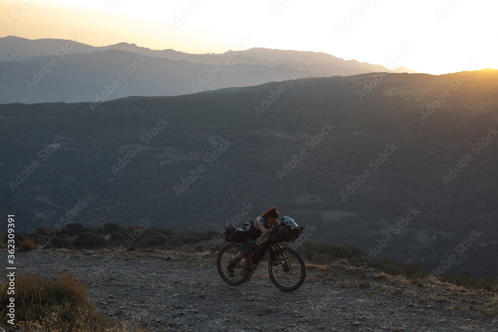 Obraz premium A bikepacker pushes her bike uphill at dusk.