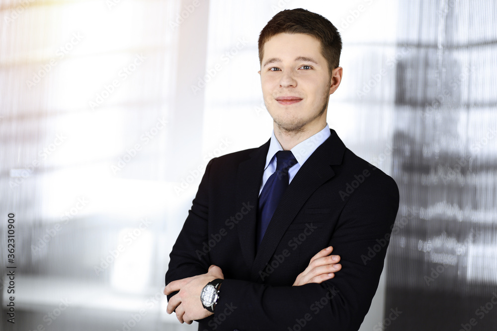 Young businessman in a suit, while standing in a sunny office. Business success concept nowadays Young businessman in a suit, while standing in a sunny office. Business success concept nowadays