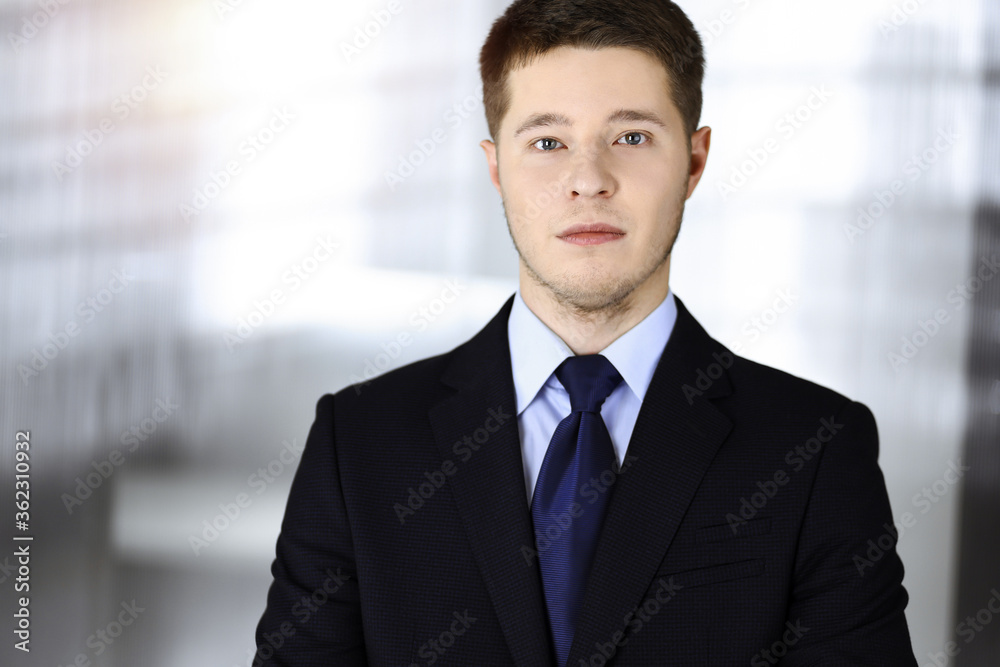 Young businessman in a suit, while standing in a sunny office. Business success concept nowadays Young businessman in a suit, while standing in a sunny office. Business success concept nowadays