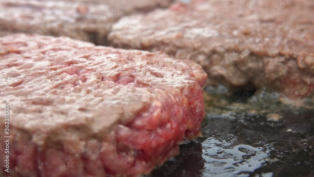 Close-up of delicious beef cutlets for a burger frying on the flat grill surface. Ingredients for hamburger preparation on the table. Close-up of delicious beef cutlets for a burger frying on the flat grill surface. Ingredients for hamburger preparation on the table.