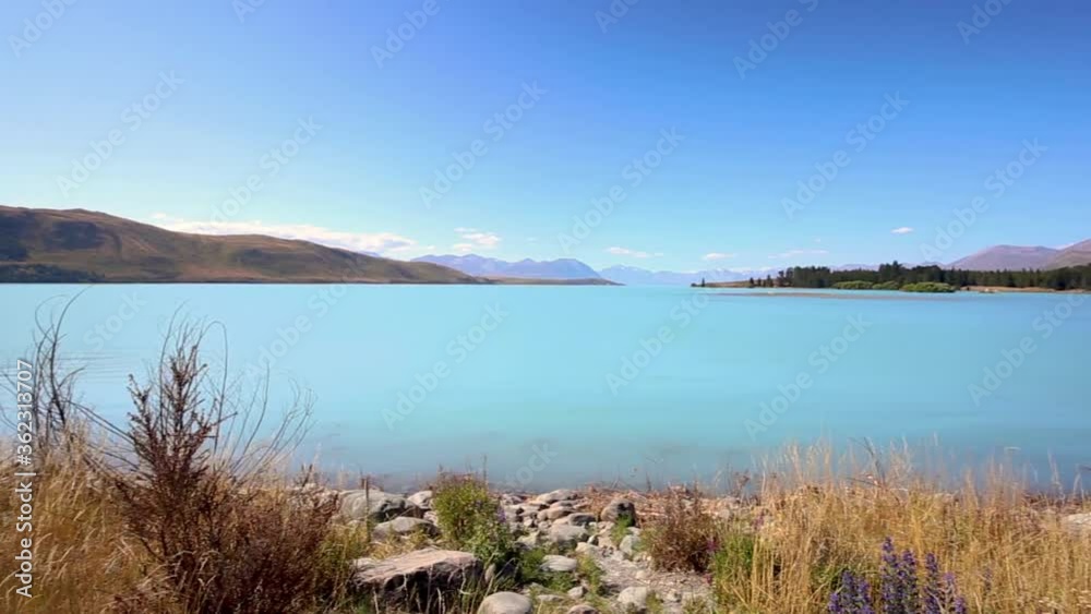 Lake Tekapo on sunny day with mountains, wide shot pan right Lake Tekapo on sunny day with mountains, wide shot pan right