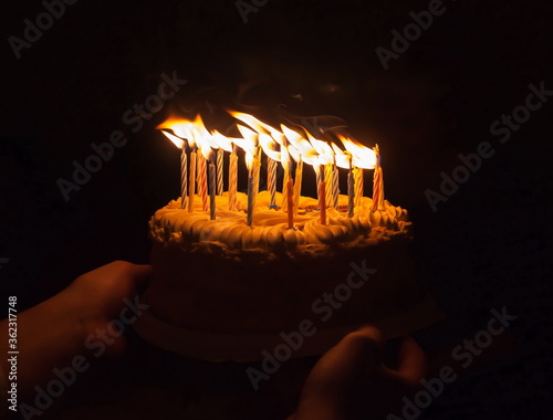 Anniversary cake with burning candles on dark background