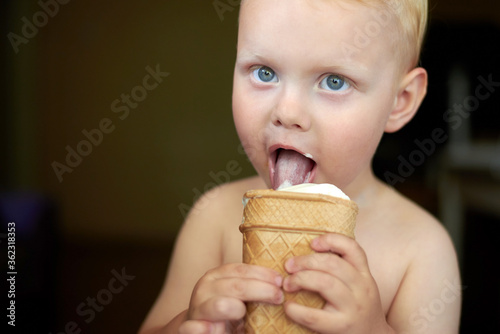 Little blue-eyed fair-haired boy eats ice cream.
