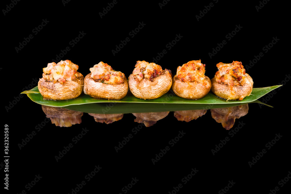 Delicious filled mushrooms with a mix of cheese and bacon with reflection, isolated on black background Delicious filled mushrooms with a mix of cheese and bacon with reflection, isolated on black background